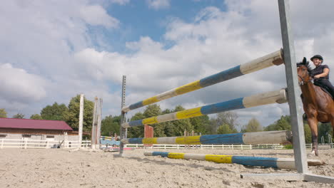 Side-view-of-a-horse-jumping-over-hurdles-on-a-cloudy-day,-low-angle-shot