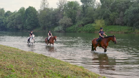 Riders,-three-young-women-riding-horses-down-the-river,-wide-shot