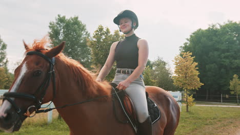 Smiling-girl-in-equestrian-outfit-enjoying-riding-horseback,-handheld-shot