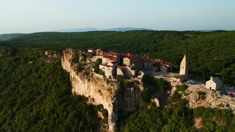 Castle-and-village-monastery-overlooking-cliff-down-onto-mountain,-Lubenice-Croatia,-aerial-orbit