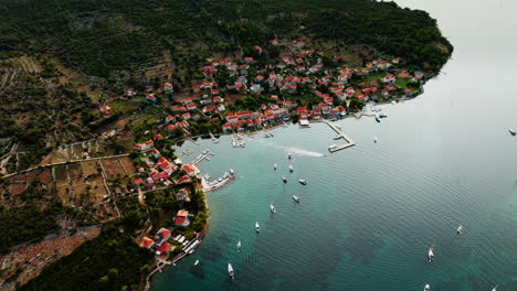 Aerial-panoramic-establishing-overview-of-Ilovik-island-Croatia-coastline,-boats-anchored-in-water-below-village