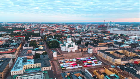 Helsinki-Cathedral-and-central-Helsinki-in-sunrise,-city-and-forest-in-background,-camera-orbiting-high