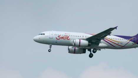 Airbus-De-Thai-Smile-Airways-Casi-Aterriza,-Revelando-Una-Torre-De-Control-De-Tráfico-Aéreo-Al-Fondo-En-El-Aeropuerto-De-Suvarnabhumi-En-Bangkok,-Tailandia,-Con-Las-Ruedas-Bajadas.