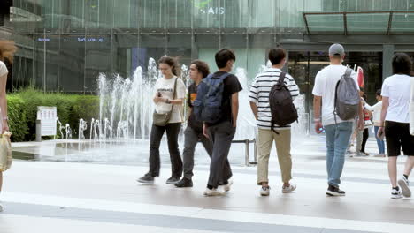 People-are-busy-walking-outside-of-Siam-Paragon-in-Bangkok-with-the-BTS-train-station-with-trains-leaving-and-stopping-for-passengers,-in-Thailand