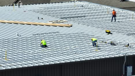 Workers-in-fluorescent-shirts-on-metal-industrial-roof-installing-metal-tracks-for-solar-panel-array