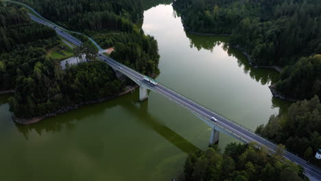 Cars-and-semi-trucks-cross-over-bridge-spanning-green-river-and-lush-forest