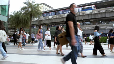 La-Gente-Está-Ocupada-Caminando-Fuera-De-Siam-Paragon-En-Bangkok-Con-La-Estación-De-Tren-BTS-Con-Trenes-Que-Salen-Y-Paran-Para-Pasajeros,-Tailandia