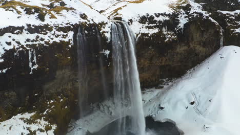 Aerial-view-of-birds-circling-a-waterfall,-in-snowy-Iceland---rising,-drone-shot