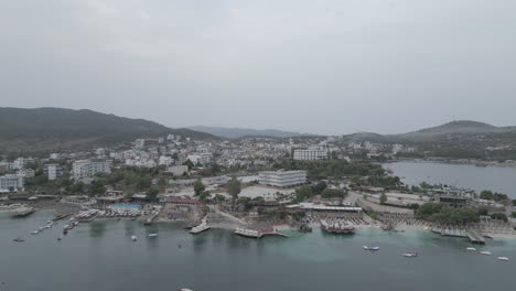 Drone-shot-flying-over-Ksamil-Albania-in-the-morning-on-a-cloudy-grey-day-with-haze-in-the-sky-and-white-hotels-and-houses-in-the-background-with-mountains-and-the-sea-LOG