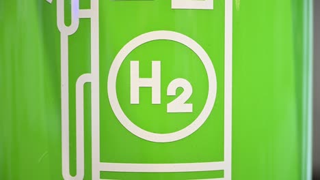 The-pictogram-of-a-hydrogen-filling-station,-fuel-pump-on-green-background,-zoom-in-on-H2-logo