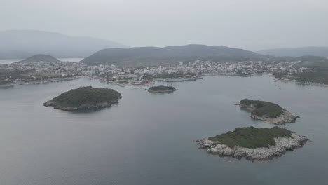 Drone-shot-flying-over-the-water-over-the-small-islands-in-front-of-Ksamil-Albania-in-the-morning-on-a-cloudy-grey-day-with-boats-around-and-haze-in-the-sky-LOG