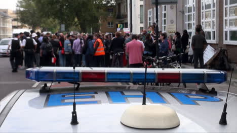 A-group-of-protestors-gathering-outside-a-courthouse-are-seen-across-the-top-of-a-police-car-as-a-red-bus-and-other-vehicles-pass-by-on-a-busy-road