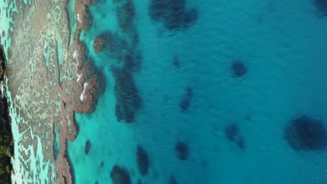 Slow-aerial-tilt-up-above-crystal-water-revealing-Maré-island'svcoastline,-New-Caledonia