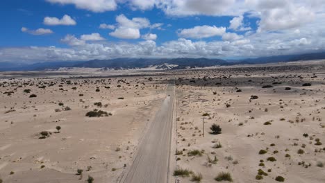 Drone-shot-following-a-car-driving-through-the-Tatón-desert-in-Catamarca,-Argentina-on-a-dusty-road
