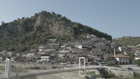 Drone-shot-of-the-city-of-Berat-and-its-castle-and-fortress-in-Albania,-the-city-of-a-thousand-windows-on-a-sunny-day-in-the-valley-with-blue-sky-with-white-houses-near-the-mountains-LOG