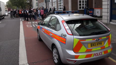 Ein-Polizeiauto-Parkt-In-Der-Nähe-Der-Stelle,-An-Der-Sich-Demonstranten-Vor-Einem-Gerichtsgebäude-Versammeln,-Während-Fahrzeuge-Auf-Einer-Stark-Befahrenen-Straße-Vorbeifahren