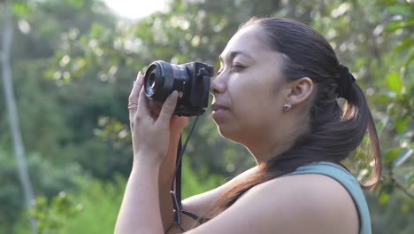 Photographer-woman-with-a-camera-in-her-hands,-taking-photographs-outdoors-surrounded-by-nature-in-the-forest