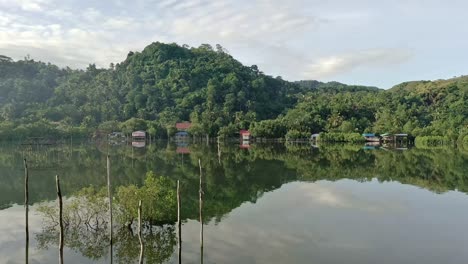 Scenic-views-of-a-fishpond-surrounded-by-lush-forests,-where-the-tranquil-waters-perfectly-mirror-the-natural-beauty-of-the-surroundings-from-an-aerial-drone-pull-out-shot