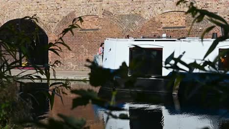 Zooming-in-to-see-people-walking-in-behind-the-boat-on-Regents-Canal,-London,-United-Kingdom