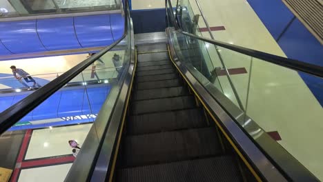 pov-shot-of-automatic-step-elevator,-camera-coming-down-automatic-stairs-where-people-are-shopping-in-shopping-mall