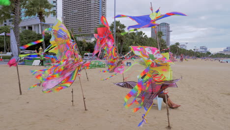 Kites-of-different-designs-and-sizes-are-tied-to-polls-to-display-how-they-fly-so-it's-easy-to-buy-and-choose-at-a-beach-with-hotels-and-condos-on-a-coastal-road-in-Pattaya,-Thailand