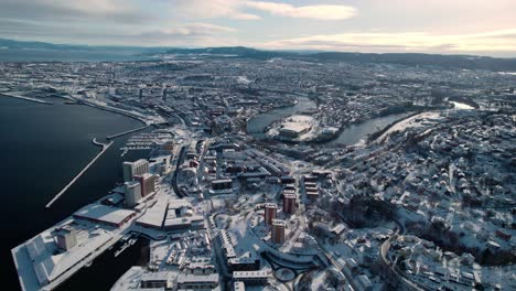 Aerial-drone-forward-moving-shot-over-city-houses-covered-with-thick-white-snow-in-Trondheim,-Norway-on-a-cold-winter-day