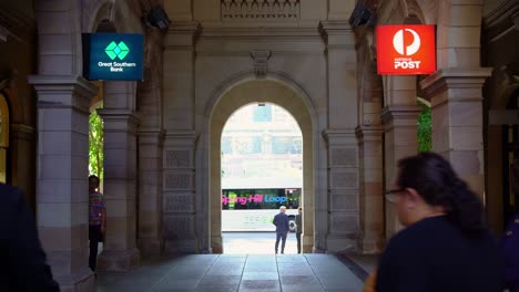 Static-shot-of-office-workers-crossing-GPO-laneway-between-Queen-and-Elizabeth-street-during-lunch-time-rush-hours-with-Anzac-square-and-central-station-in-the-background-through-the-archway