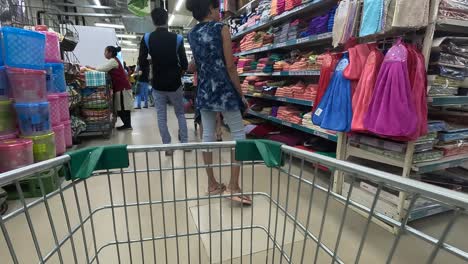 WIDE-SCENE,-POV-SHOT-OF-EMPTY-SHOPPING-BASKET,-shopping-basket-moving-forward-in-super-mall-with-people-shopping,-people-buying-daily-household-items