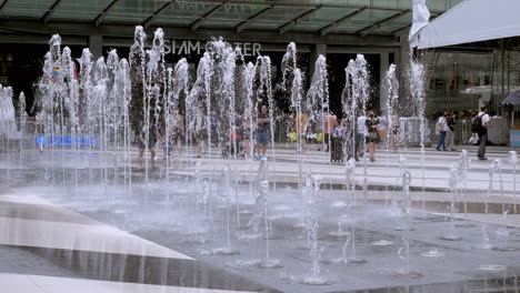 People-walking-by-at-the-background-of-this-landmark-of-a-water-fountain-in-front-of-Siam-Center-and-Siam-Paragon-in-Bangkok,-Thailand