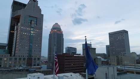 Banderas-De-Estados-Unidos-Y-Kentucky-Ondeando-Frente-Al-Horizonte-Del-Centro-De-Louisville,-Ky-Al-Amanecer