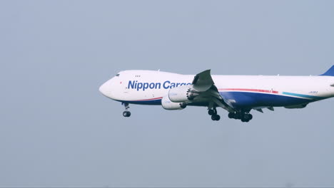 Nippon-Frachtflugzeug-Mit-Heruntergeklappten-Rädern-Beim-Aufsetzen-Auf-Dem-Rollfeld,-Vorbeifliegend-Am-Flugsicherungsturm,-Lichtmasten,-Bäumen-Und-Gras,-Am-Flughafen-Suvarnabhumi-In-Bangkok,-Thailand