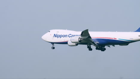 Avión-De-Carga-Japonés-Con-Las-Ruedas-Abajo-Capturado-Aterrizando-En-La-Pista-Volando-Junto-A-La-Torre-De-Control-Del-Tráfico-Aéreo,-Postes-De-Luz,-árboles-Y-Césped,-En-El-Aeropuerto-De-Suvarnabhumi-En-Bangkok,-Tailandia