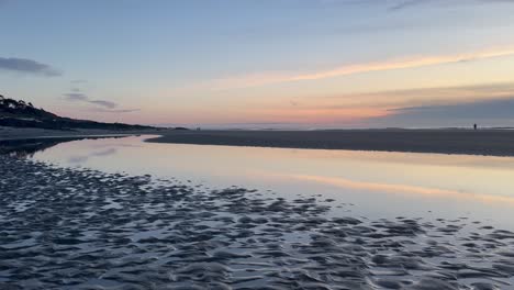 A-couple-walking-past-the-pool-reflecting-the-sunset-on-the-Oregon-coast-beach