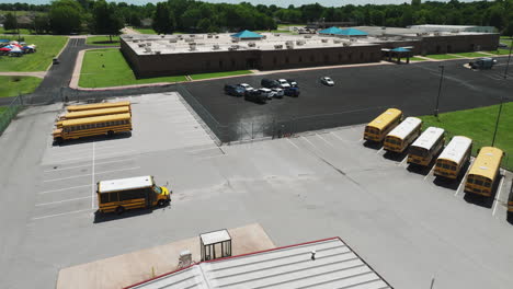 Aerial-View-Of-Yellow-School-Bus-Parked-In-The-Parking-Lot-Of-School-In-Siloam-Springs,-Arkansas