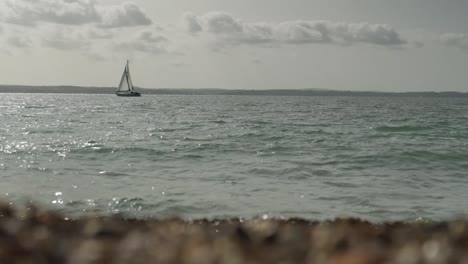 Boat-floats-on-the-sea,-with-waves-crashing-into-pebbles-in-the-foreground