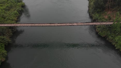 Old-wooden-suspension-bridge-crossing-a-river-at-Vietnam,-aerial