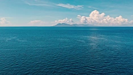 Eine-Luftdrohne,-Die-über-Die-Wasseroberfläche-Aufsteigt,-Entfaltet-Einen-Malerischen-Ozeanlandschaftshorizont-Mit-Einer-Fernen-Insel-Am-Horizont,-Den-Philippinen
