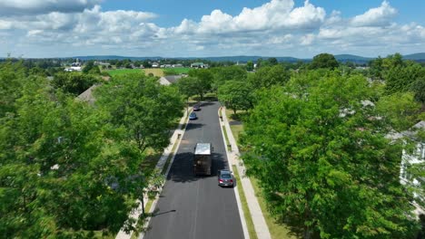 UPS-truck-driving-through-upscale-American-neighborhood-lined-with-mature-trees-on-summer-day