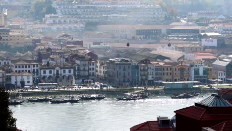Cable-cars-traverse-in-sky-above-Rabelo-boats-anchored-in-Douro-river,-Porto