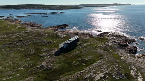 Long-Studio-Modern-Architecture-Overlooking-Atlantic-Views-with-Glistening-Sunlight-Reflecting-on-Fogo-Island-from-an-Aerial-Tilt-Down-Push-In-Drone-Shot,-Newfoundland,-Canada