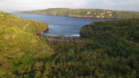Aerial-Sunrise-Flying-Over-Hilly-Tropical-Forest-Revealing-Gamat-Bay-Beach-in-Nusa-Penida,-Bali,-Indonesia
