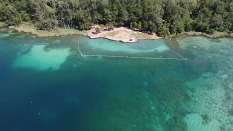 Drohnen-Luftaufnahmen-Eines-Natürlichen,-Von-Wald-Umgebenen-Sees-In-Spanien,-In-Dem-Menschen-Schwimmen