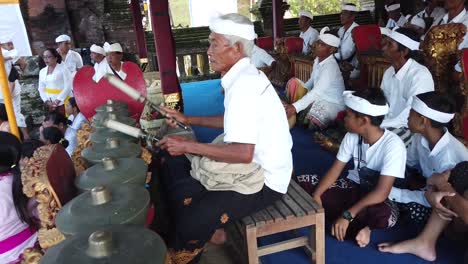 Traditional-Orchestra-Plays-Gamelan-Music-at-Hindu-Temple-Ceremony-in-Bali-Indonesia,-Elder-Musicians-and-Local-Family-in-Gianyar