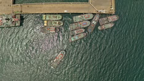 A-group-of-tugboats-pulling-a-large-barge-docked-next-to-a-concrete-pier-at-nickel-Mines-in-Taganito,-Philippines