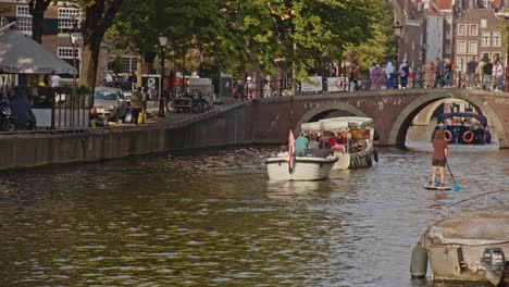 Static-view-of-beautiful-canal-in-Amsterdam-with-small-boats-and-a-sup-paddler