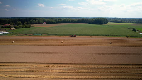 Aerial-trucking-shot-of-tractor-harvesting-corn-and-cereal-on-farm-field-during-sunny-day