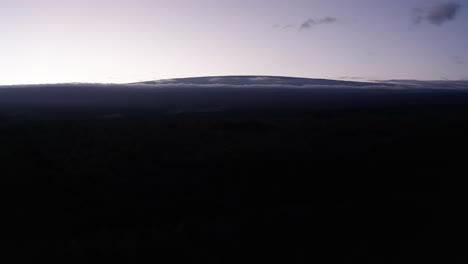 Aerial-reverse-pullback-descending-shot-of-Mauna-Loa-towering-above-the-clouds-at-sunset-in-Hawai'i