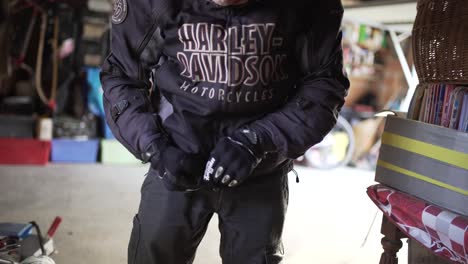 Harley-Davidson-biker-puts-on-protection-gloves-and-closes-jacket-in-his-garage