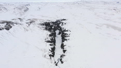 Aerial-view-away-from-a-snowy-gorge,-winter-in-cloudy-Iceland---pull-back,-drone-shot