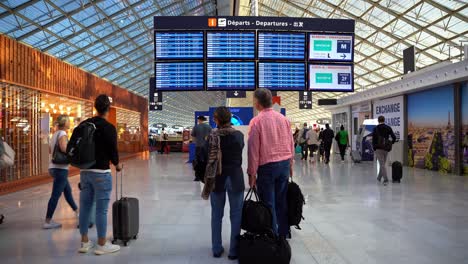 Grupo-De-Personas-Con-Equipaje-Preparándose-Para-Viajar-Mirando-Las-Pantallas-Anunciando-Sus-Vuelos,-El-Aeropuerto-De-París,-Francia